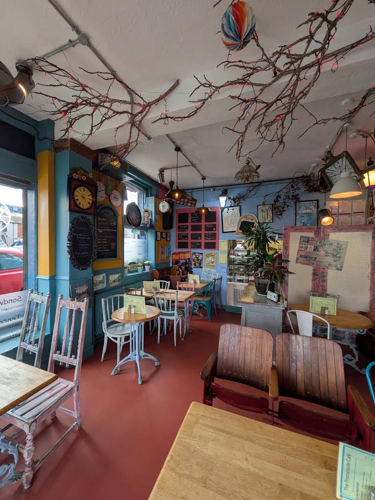 The café’s colourful interior, with pink and blue wooden chairs, wooden seats and branches with lights across the ceiling